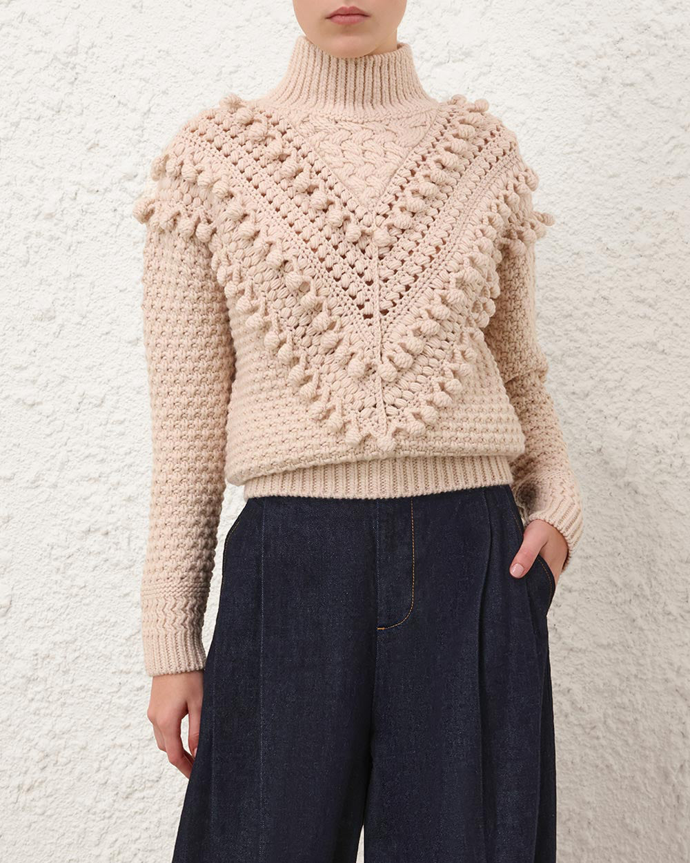 Person wearing a beige knitted sweater with a textured pattern against a white background